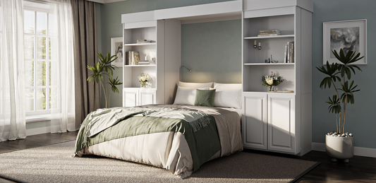A pull-down white Murphy bed framed by matching built-in bookcases and lower storage cabinets in a sunlit bedroom.